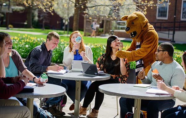 The Nittany Lion mascot serving icecream to students seated at an outdoor patio