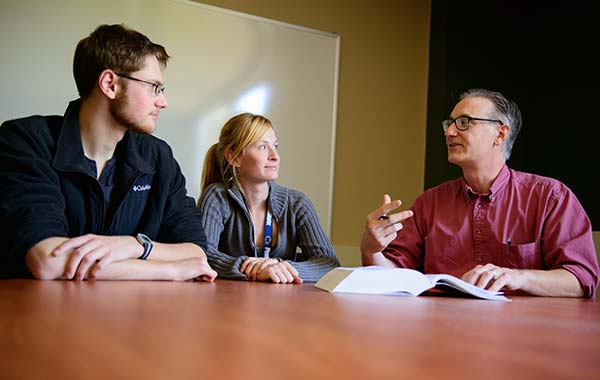 Two students, one male and one female, seated at a desk meeting with a faculty member