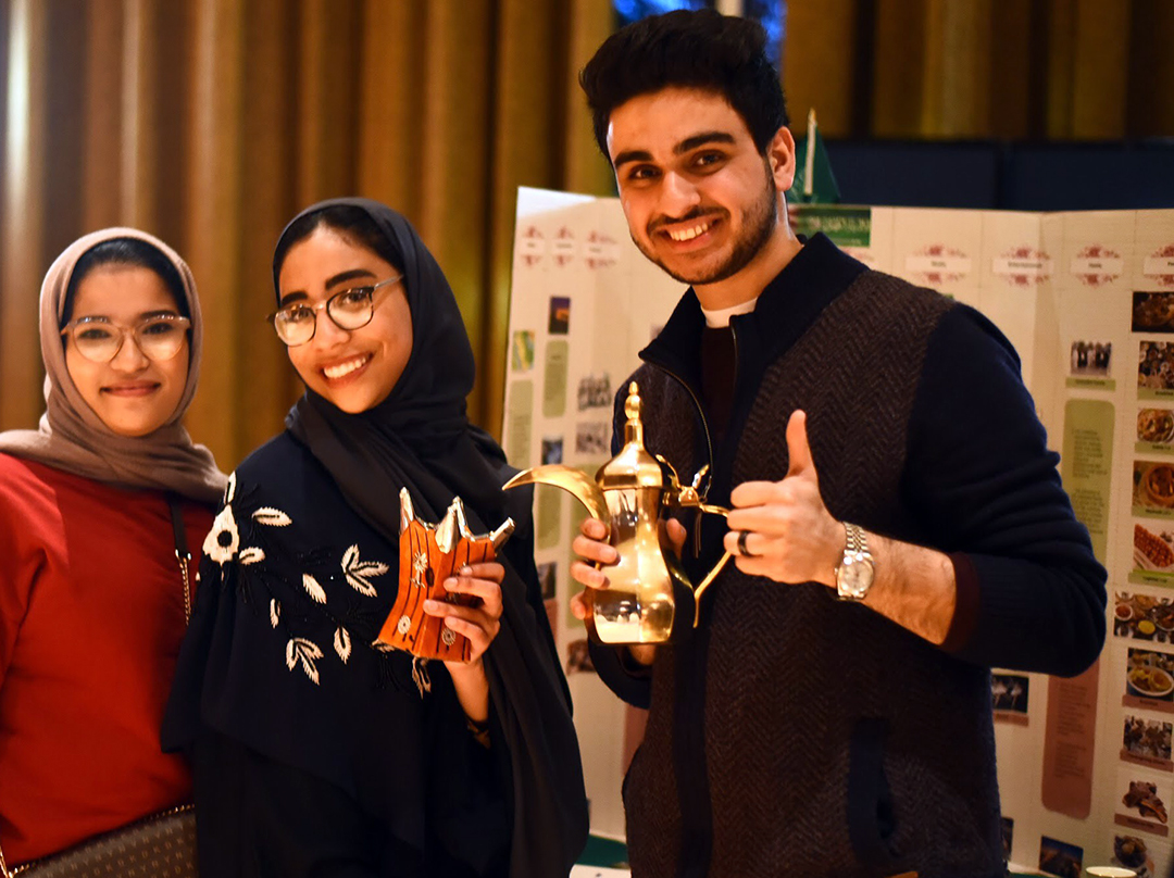 Three happy international students with cultural artifacts and Academic Poster